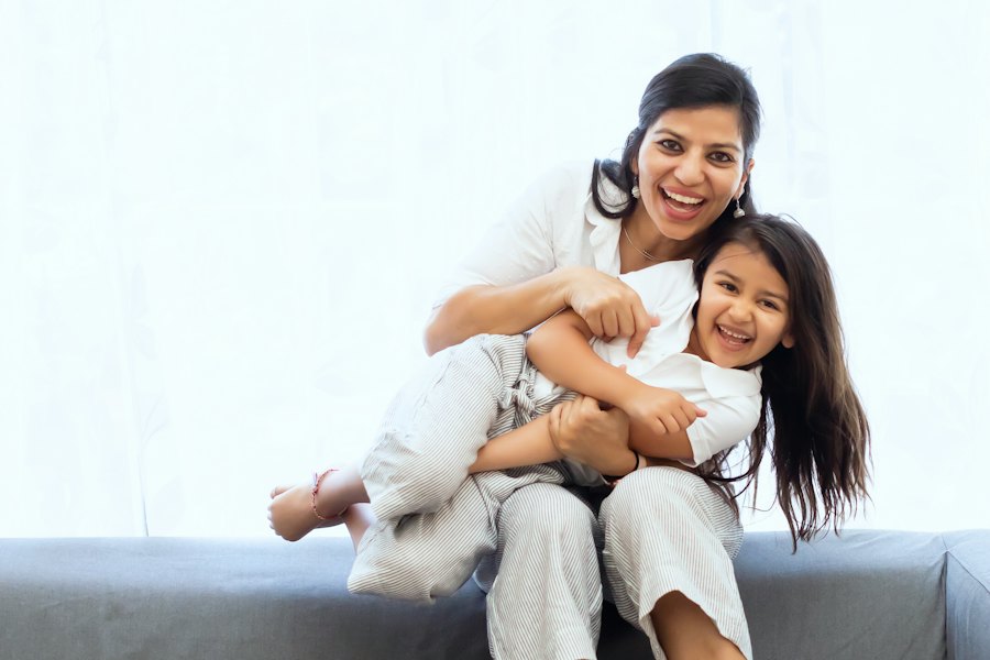 A mother laughing with her young daughter on the sofa